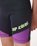 Detalle del logo Rip Curl en la pierna del traje de neopreno Grom's Omega 1.5mm niño, color negro, verde y morado.