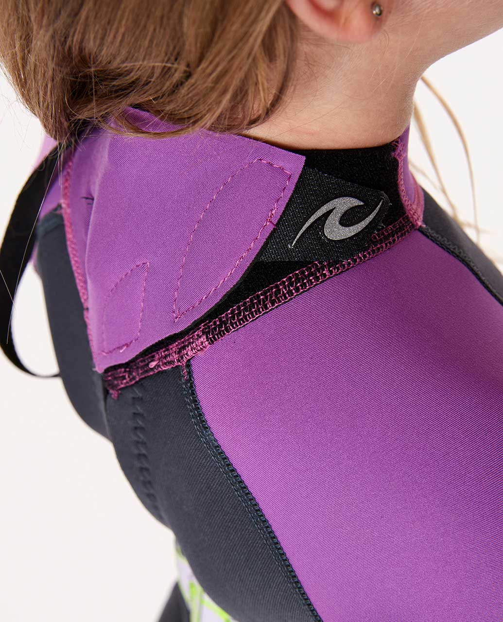 Detalle del cuello y cremallera trasera del traje de neopreno Rip Curl Grom's Omega 1.5mm niño, cierre con velcro, costuras reforzadas, color morado y negro.