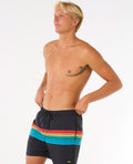 Modelo ajustando el bañador Rip Curl Surf Revival Volley 16'', ideal para surf y playa, confeccionado con poliéster reciclado.