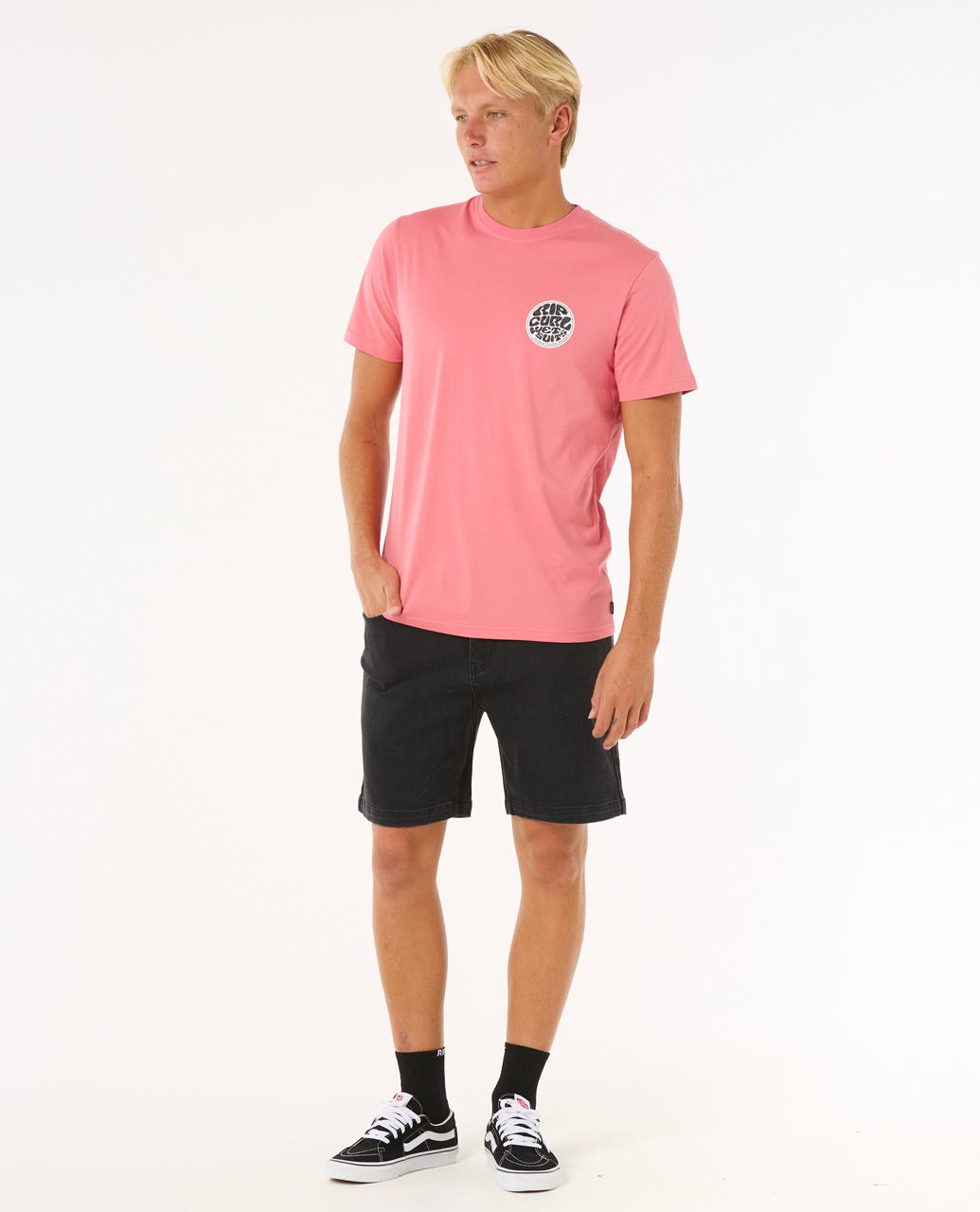 Modelo con camiseta Rip Curl Wettie Passage Icon Tee rosa y shorts negros, look casual veraniego.