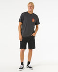 Camiseta Rip Curl Shaper Address Tee negra jaspeada, look completo con pantalón corto negro y zapatillas.