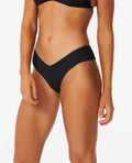 Braga de bikini Rip Curl Premium Surf Skimpy Hipster negra, vista lateral, diseño favorecedor en V y tejido reciclado.