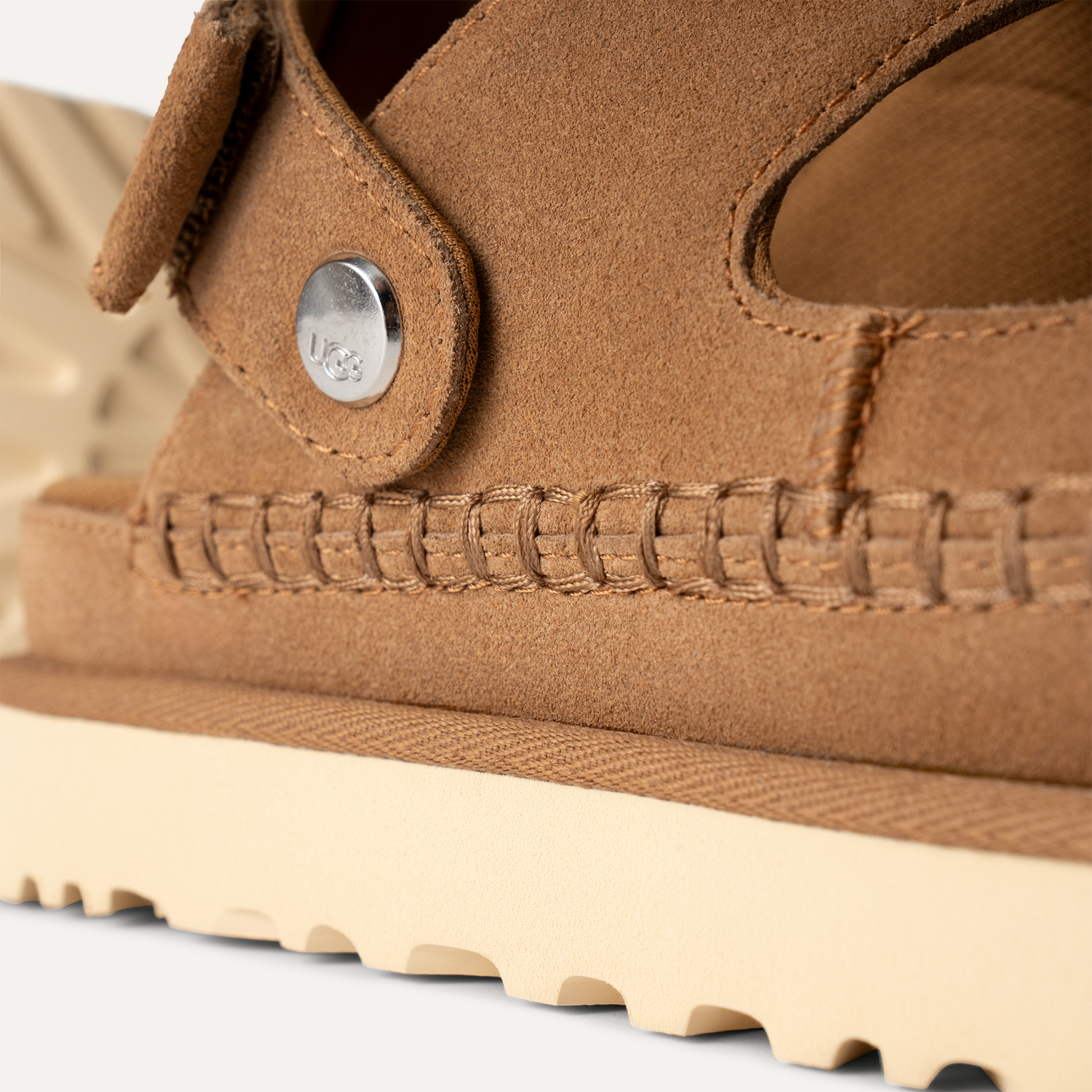 Detalle del empeine de ante marrón claro y costura artesanal de las sandalias UGG Goldenstar Glide para mujer
