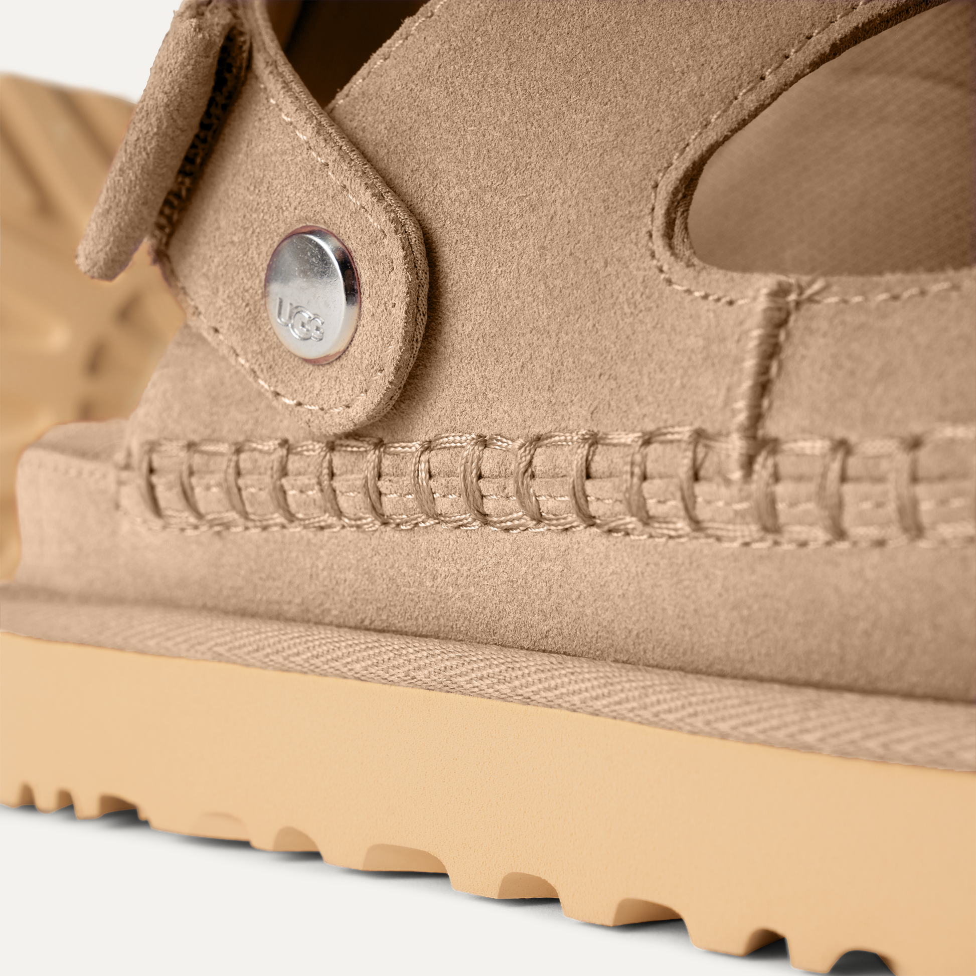 Detalle del empeine de ante marrón claro y costura artesanal de las sandalias UGG Goldenstar Glide para mujer