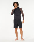 Modelo de cuerpo completo con camiseta Rip Curl Search UPF Performance L/S Hood y shorts, ideal para surf y deportes acuáticos