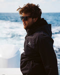 Hombre usando la chaqueta Salty Crew Long Range Jacket negra en un barco, con cremallera impermeable y diseño ideal para aventuras náuticas.