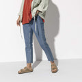 Modelo femenino con sandalias Birkenstock Arizona Plantilla Blanda cuero Tobacco Brown combinadas con vaqueros recortados y chaqueta verde salvia.
