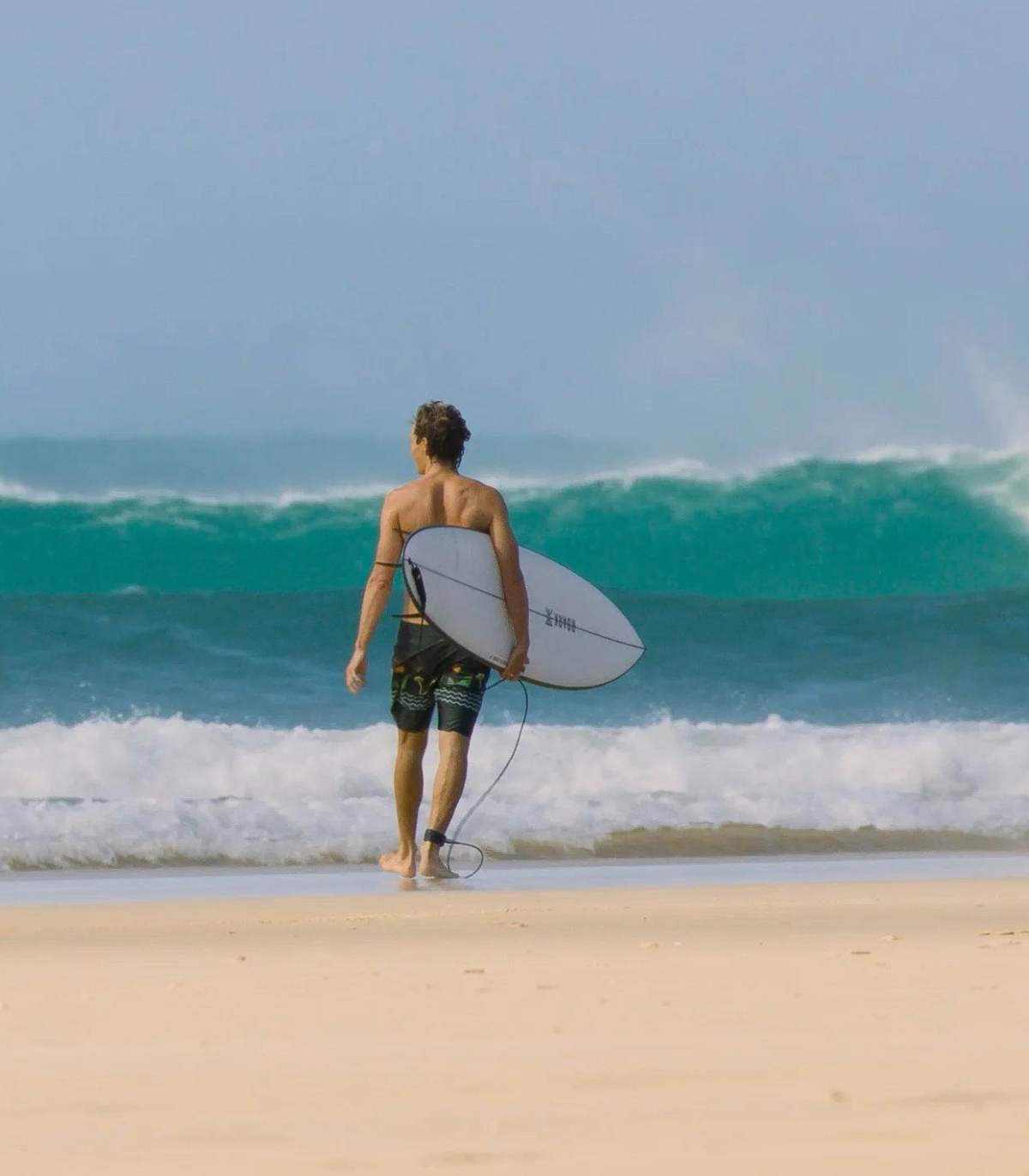 Un surfer entra al agua con la Tabla de surf JS El Baron PE Mid Length