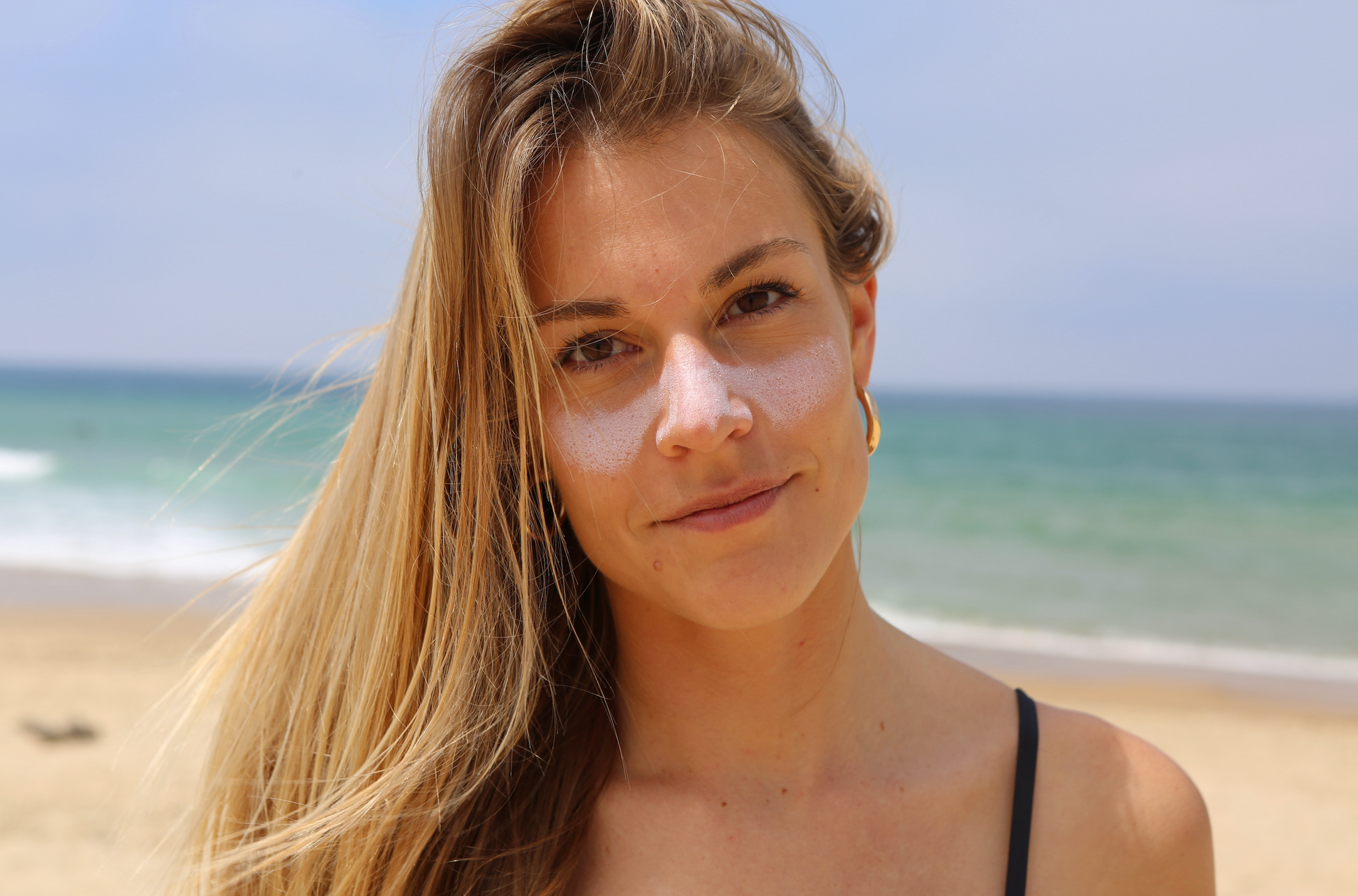 Mujer en la playa con protección solar Greenbush SPF 50+ blanca aplicada en las mejillas, fondo marino