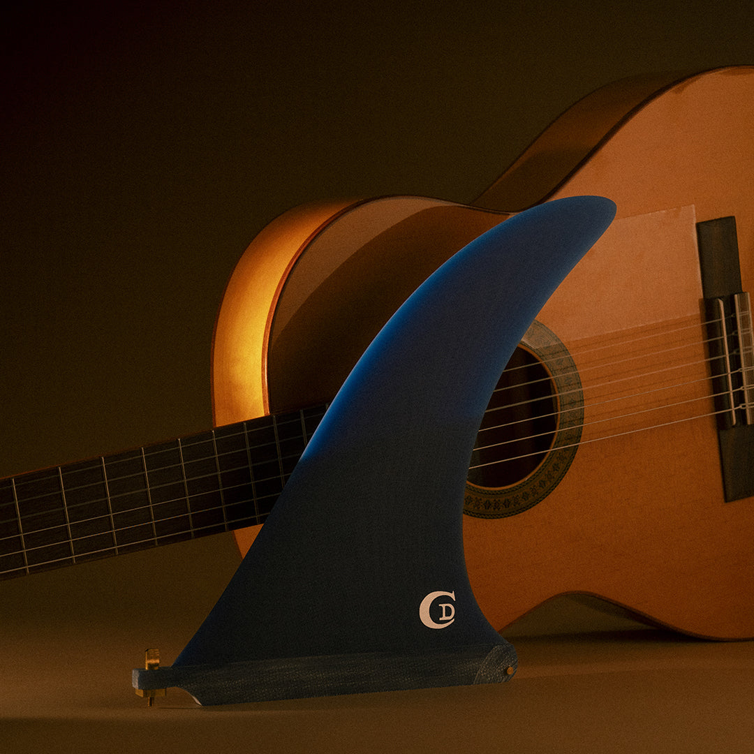 Quilla single fin Deflow Bulerías Fugue azul marino frente a guitarra flamenca, vista completa con base US Box y tornillo dorado, logo CD de Clovis Donizetti.