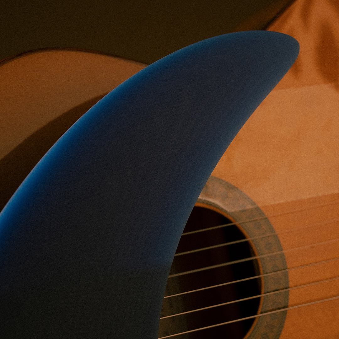 Detalle del tip de la quilla single fin Deflow Bulerías Fugue, degradado de azul marino a azul intenso con guitarra flamenca de fondo en sesión de producto.