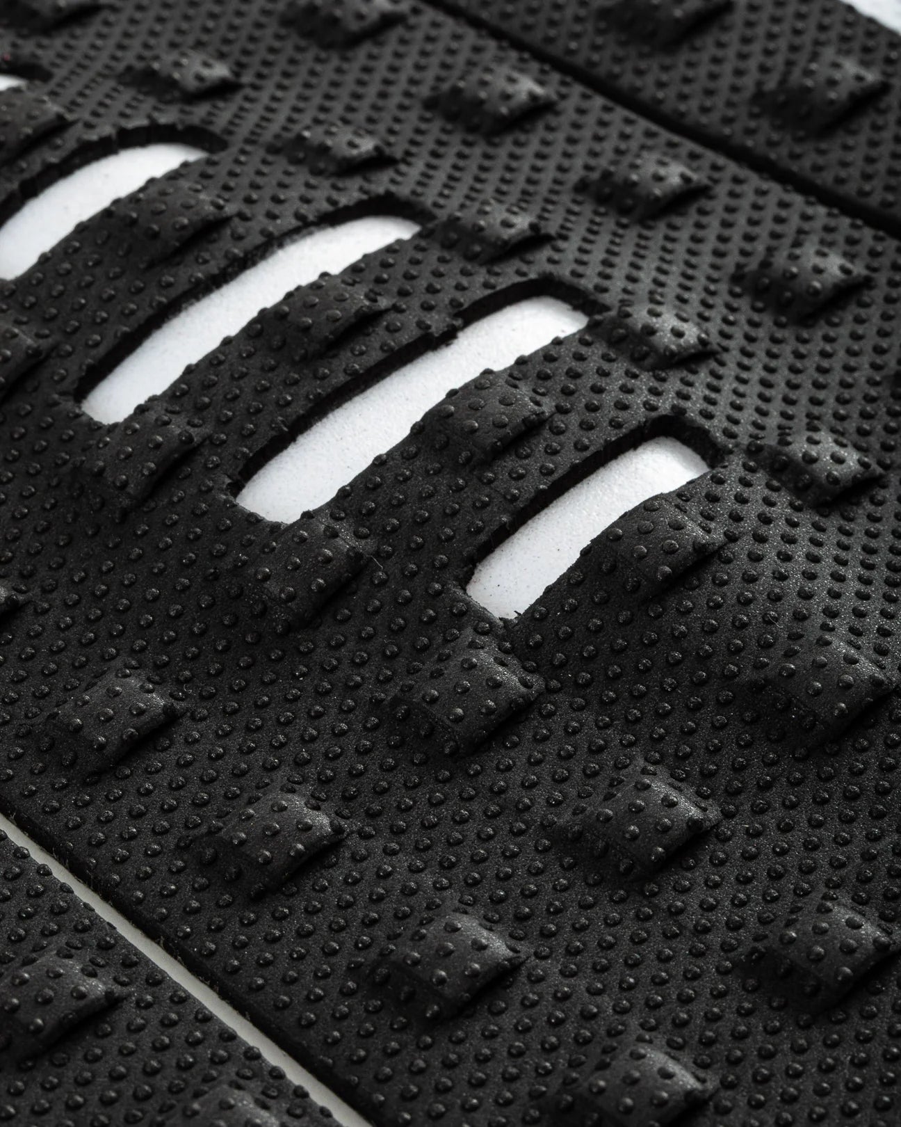 Detalle de los cortes estratégicos blancos en el patrón Square Loc negro del grip Creatures Mick Eugene Fanning Signature black white para máximo contacto del pie en tablas alternativas.