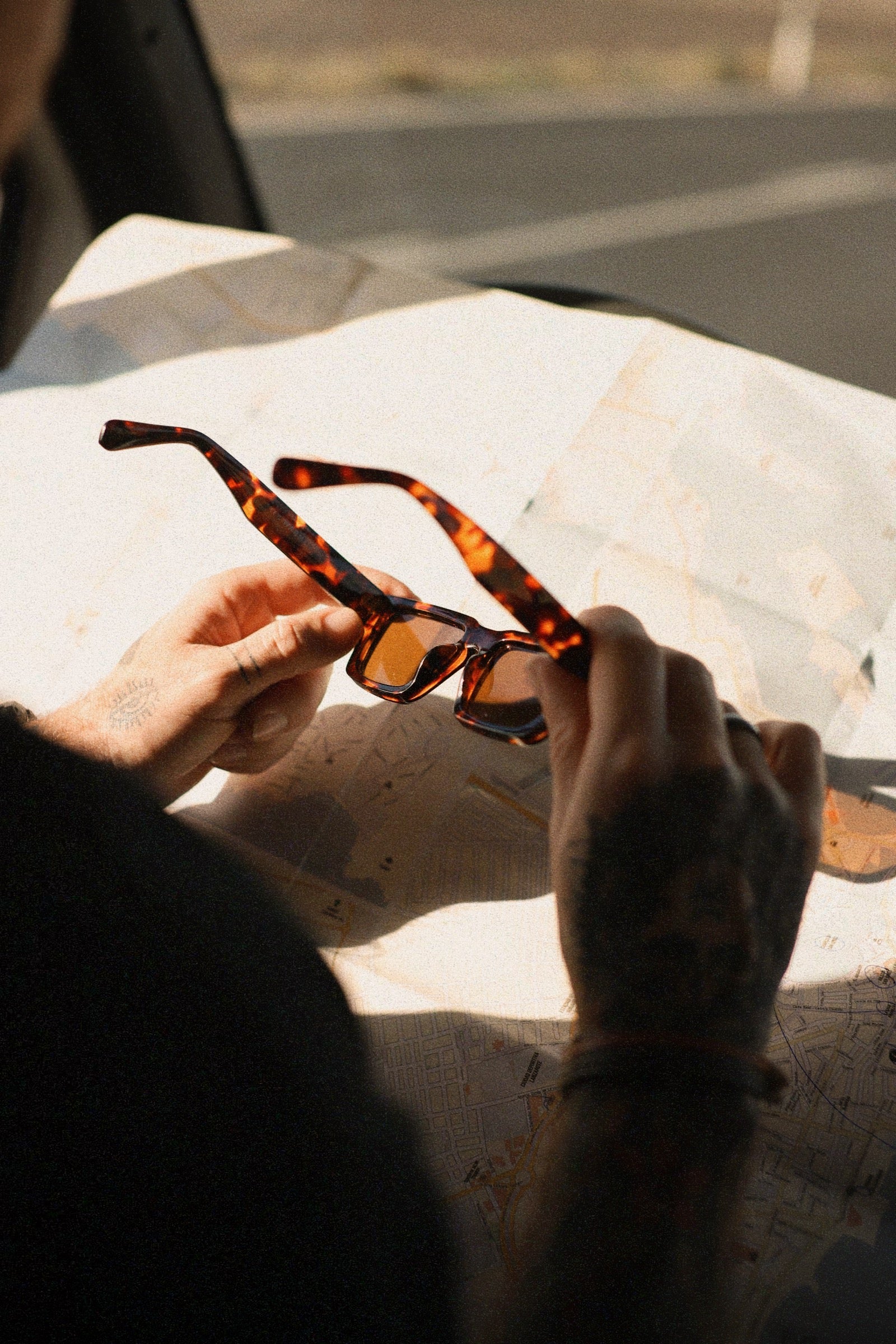 Manos sosteniendo gafas de sol Warmouth Eyewear Rusty Rooms sobre mapa, detalle de montura de acetato color carey y lentes marrones