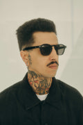 Hombre con tatuajes vistiendo gafas de sol Warmouth Eyewear Kelly Kook en color negro, estilo moderno y urbano