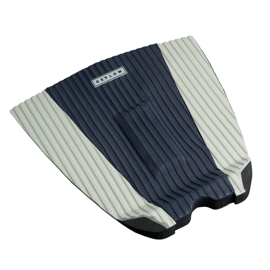Grip de surf Deflow Adrien Toyon Traction Pad azul marino y blanco sobre fondo azul, 3 piezas con acanaladuras verticales y arco central visible.