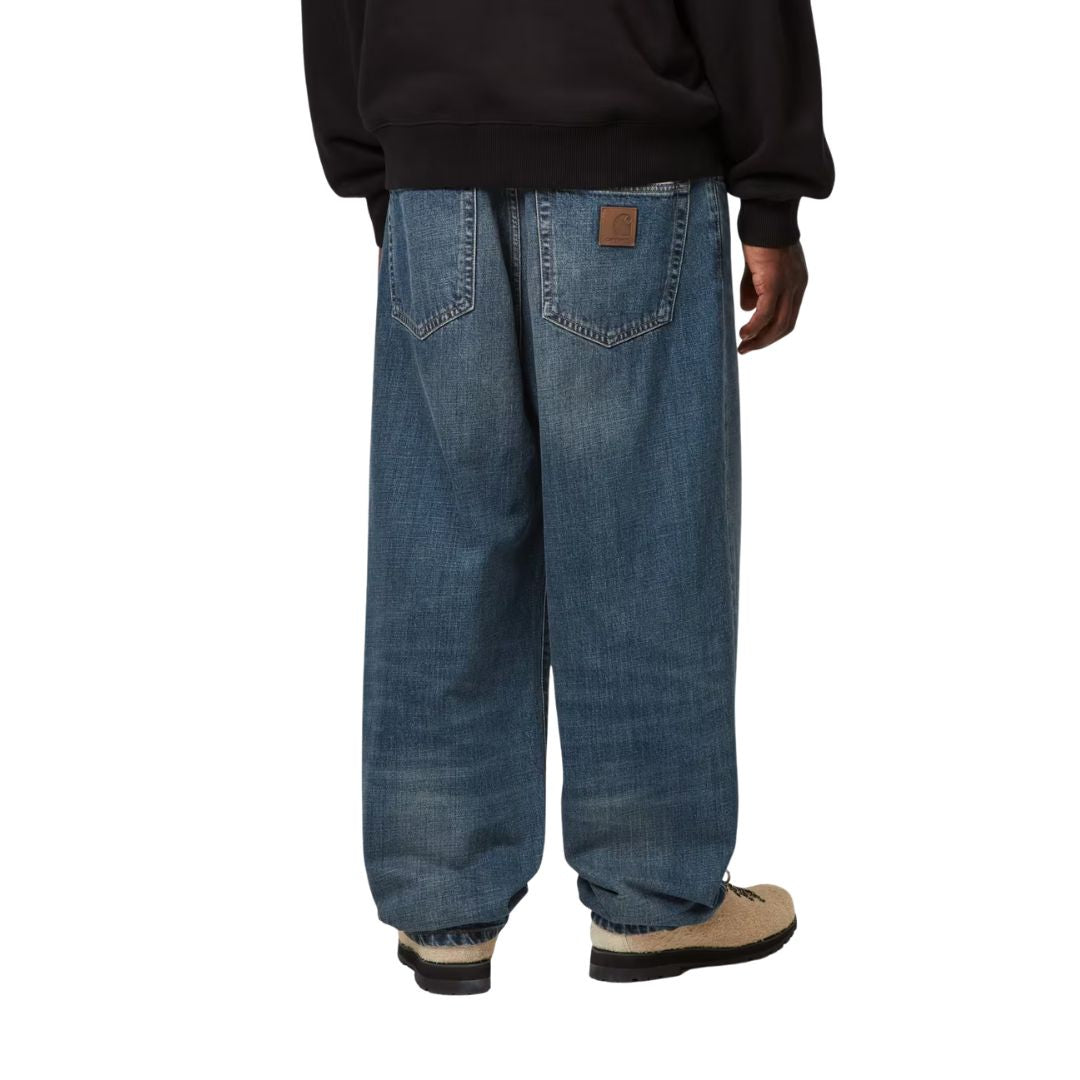 Carhartt WIP Aaron Pant Blue Stone Washed vista trasera en modelo, pantalón denim regular tapered con etiqueta cuadrada en bolsillo posterior.