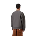 Sudadera Carhartt WIP American Script gris grafito puesta por un modelo, vista trasera, combinada con pantalón de pana marrón, mostrando el corte oversize de espalda.