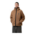 Modelo con las manos en los bolsillos y la chaqueta Carhartt WIP Blevin Liner en color WIP H Brown, forro polar con capucha, cremallera negra y cordón en el bajo.