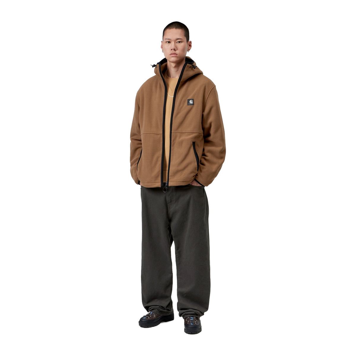 Modelo de cuerpo entero con la chaqueta forro polar Carhartt WIP Blevin Liner en color WIP H Brown, combinada con pantalón ancho verde oscuro y zapatillas negras.