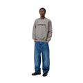 Modelo con sudadera Carhartt WIP Carhartt Sweat en gris Shady Grey y logo Dark Navy combinada con vaqueros anchos, mostrando el calce oversize y la caída relajada de la prenda.