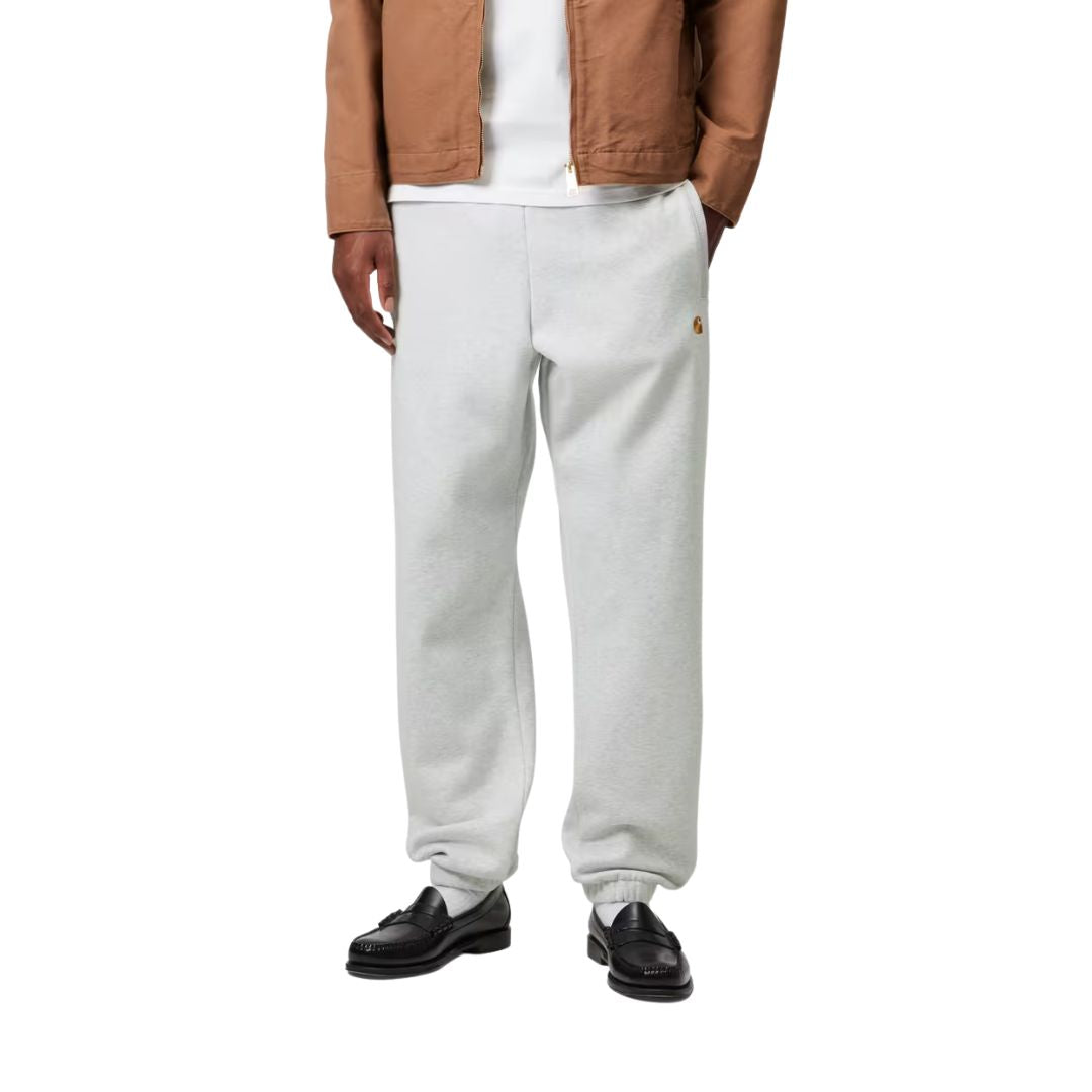 Modelo con Carhartt WIP Chase Sweat Pant en negro, primer plano frontal desde la cintura. Muestra la cintura elástica ajustable y el logo "C" bordado en dorado.