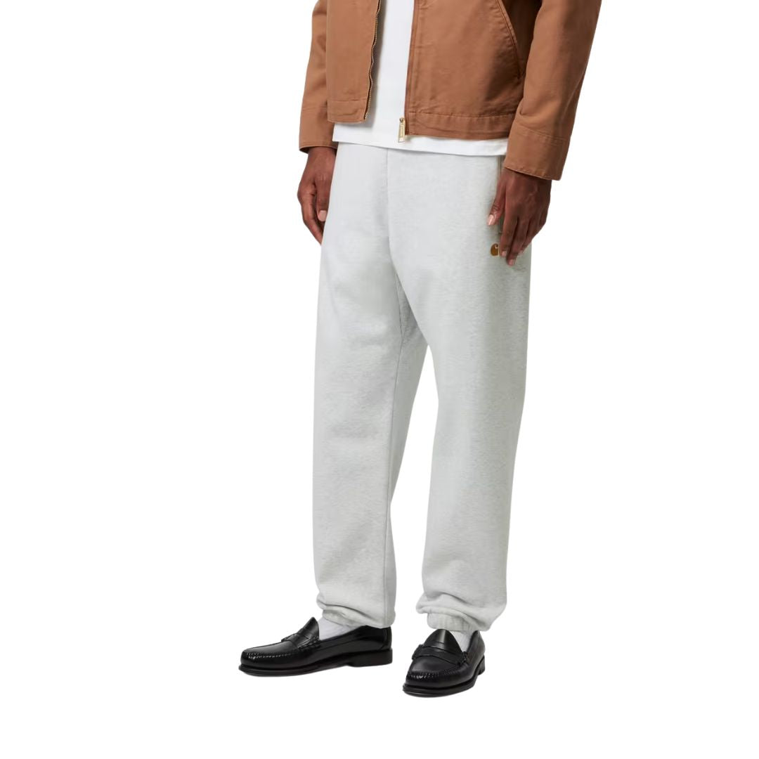 Modelo con Carhartt WIP Chase Sweat Pant en negro, primer plano lateral. Se distingue con detalle el logo "C" bordado en dorado junto al bolsillo frontal.