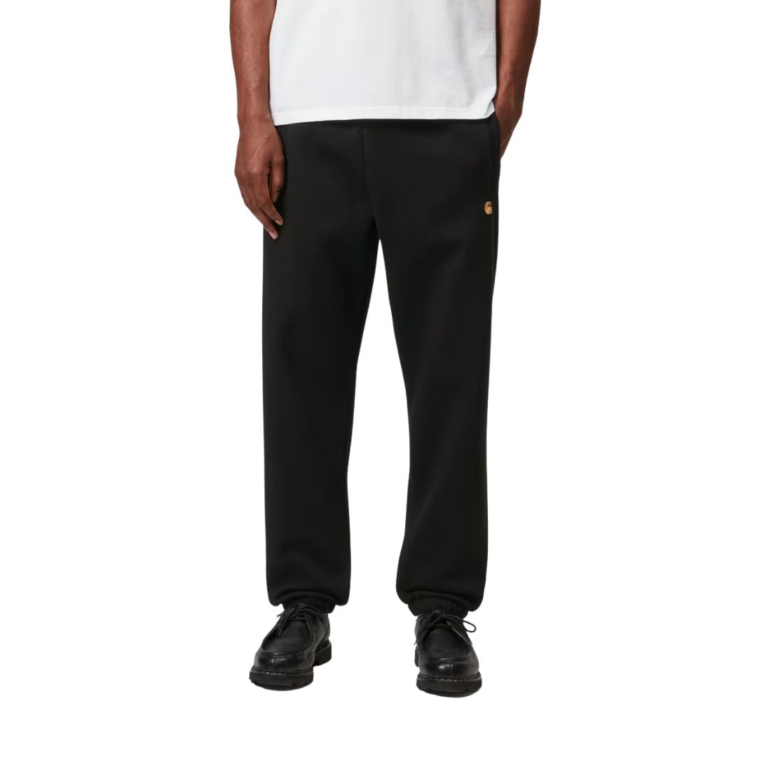 Modelo con Carhartt WIP Chase Sweat Pant en ash heather, primer plano frontal desde la cintura. Muestra la cintura elástica ajustable y el logo "C" bordado en dorado.