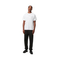 Modelo con Carhartt WIP Chase Sweat Pant en ash heather, vista frontal completa. Combina el jogger con cazadora marrón, mostrando el corte holgado y el largo del bajo.