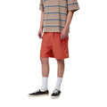 Carhartt WIP Chase Swim Trunks en color oxide red con detalle dorado, vista frontal lateral sobre modelo masculino. Bañador de poliéster ligero en rojo teja con logotipo 