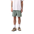 Carhartt WIP Chase Swim Trunks en color velvet green con detalle dorado, vista frontal sobre modelo masculino. Bañador de poliéster ligero en verde apagado con logotipo 