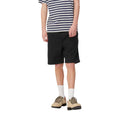Carhartt WIP Flint Short en color negro teñido en prenda, vista frontal sobre modelo masculino. Bermuda de algodón orgánico con cinturilla elástica con cordón, bolsillos frontales integrados y largo holgado sobre la rodilla. Corte regular fit.