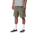 Carhartt WIP Flint Short en color verde leaf teñido en prenda, vista frontal lateral sobre modelo masculino. Bermuda de algodón orgánico con cinturilla elástica, bolsillos frontales integrados y largo por encima de la rodilla. Corte regular fit.