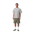 Carhartt WIP Flint Short en color verde leaf teñido en prenda, vista completa de look sobre modelo masculino. Bermuda de sarga orgánica de corte regular combinada con camisa de rayas Carhartt WIP, calcetines blancos y zapatillas Vans negras.