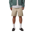 Carhartt WIP Flint Short en color wall teñido en prenda, vista frontal sobre modelo masculino. Bermuda de algodón orgánico en tono beige con cinturilla elástica, bolsillos frontales integrados y acabado garment dyed con variaciones sutiles de color. Corte regular fit.