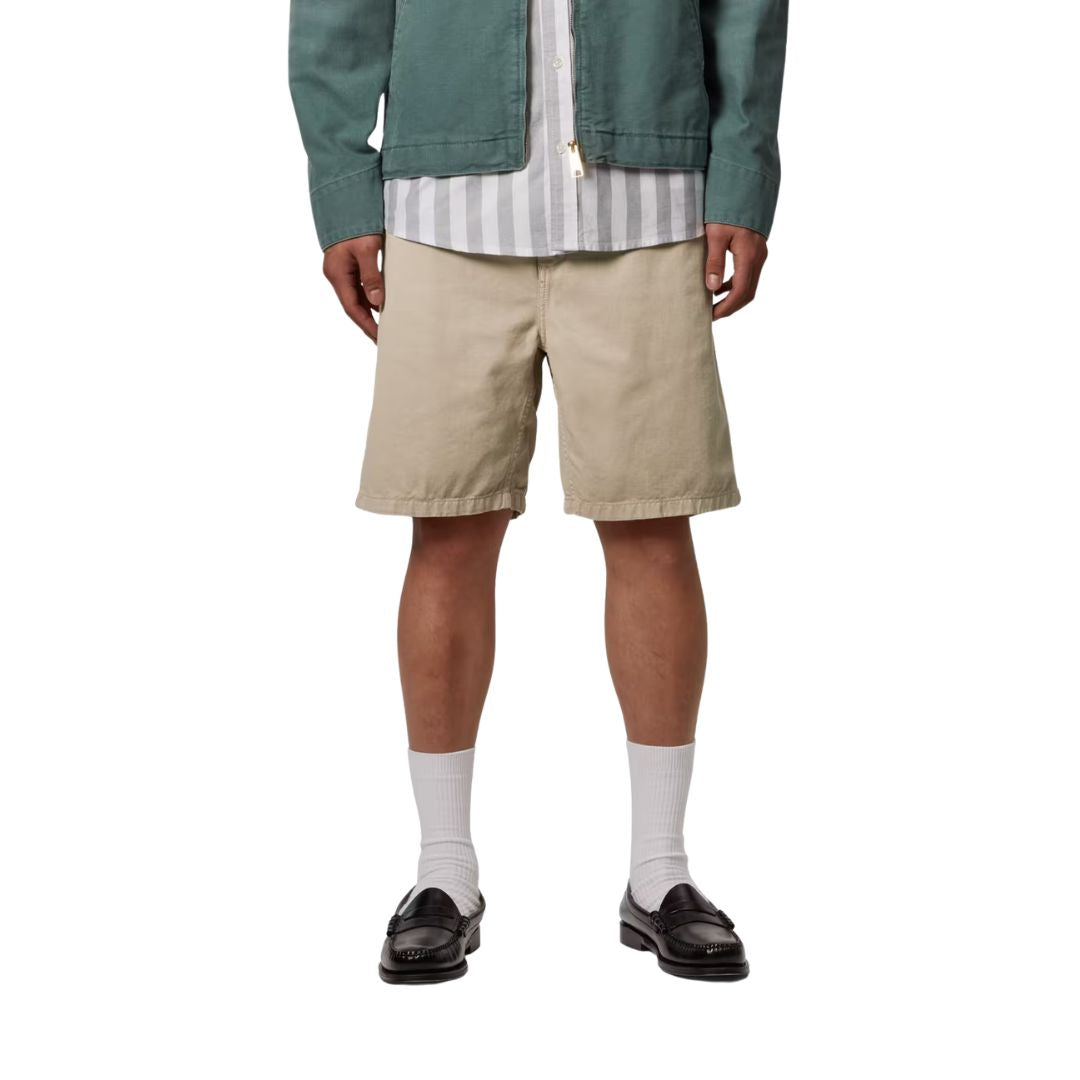 Carhartt WIP Flint Short en color wall teñido en prenda, vista frontal sobre modelo masculino. Bermuda de algodón orgánico en tono beige con cinturilla elástica, bolsillos frontales integrados y acabado garment dyed con variaciones sutiles de color. Corte regular fit.