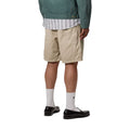 Carhartt WIP Flint Short en color wall teñido en prenda, vista trasera sobre modelo masculino. Bermuda de sarga de algodón orgánico en tono beige arena con dos bolsillos traseros de parche con puntadas de remate y bolsillo para herramientas en la pierna derecha. Corte regular fit.