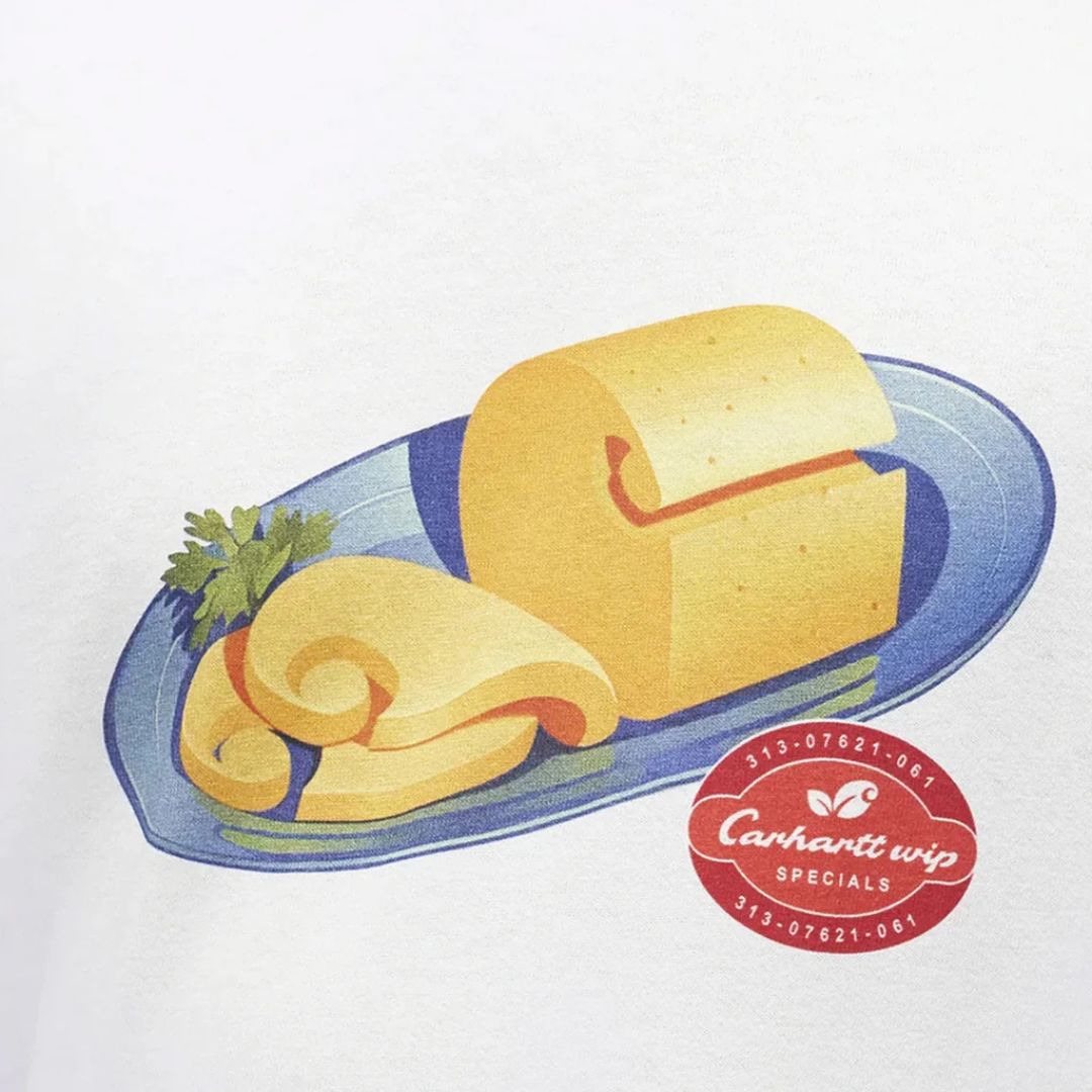 Detalle del estampado de la camiseta Carhartt WIP S/S Fromage: ilustración de una tabla de quesos sobre un plato azul con perejil, junto al parche rojo Carhartt WIP Specials 313-07621-061.