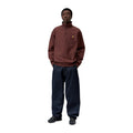 Modelo de cuerpo entero con la sudadera Carhartt WIP Half Zip American Script Sweat en color Amarone, combinada con vaqueros oscuros anchos y zapatillas negras.