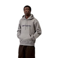Modelo con sudadera capucha Carhartt WIP Hooded Carhartt Sweat color Shady Grey y logo bordado Dark Navy, cordones ajustables al tono y bolsillo canguro frontal con manos dentro.