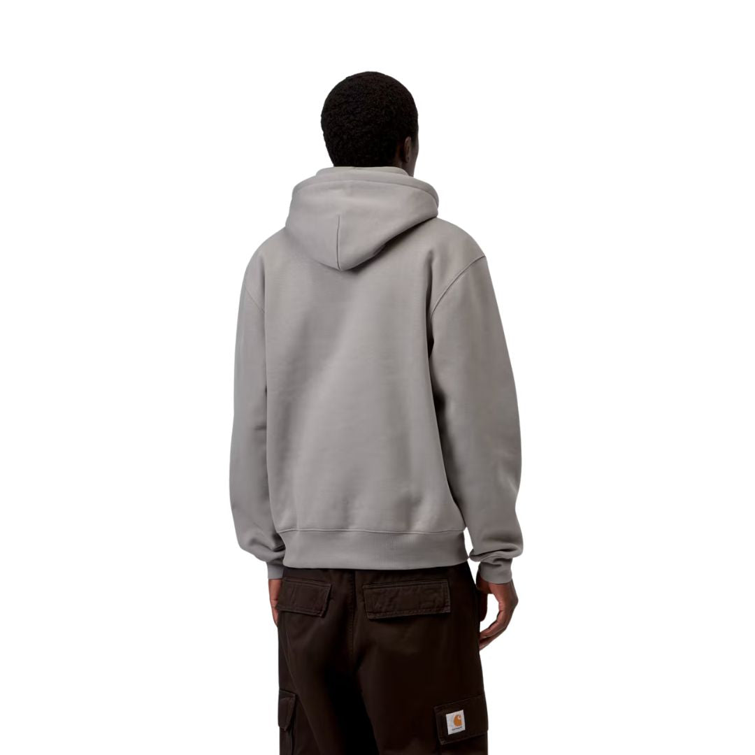 Modelo de espaldas con sudadera con capucha Carhartt WIP Hooded Carhartt Sweat en gris Shady Grey, mostrando la caída oversize, capucha forrada y puños acanalados sobre pantalón cargo oscuro.