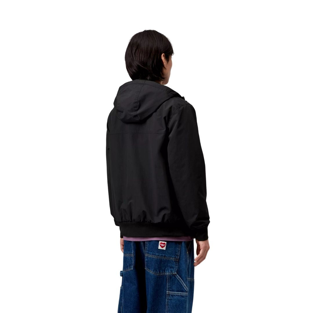 Vista trasera del modelo con la chaqueta Carhartt WIP Hooded Sail Jacket negra, mostrando la caída y corte regular.