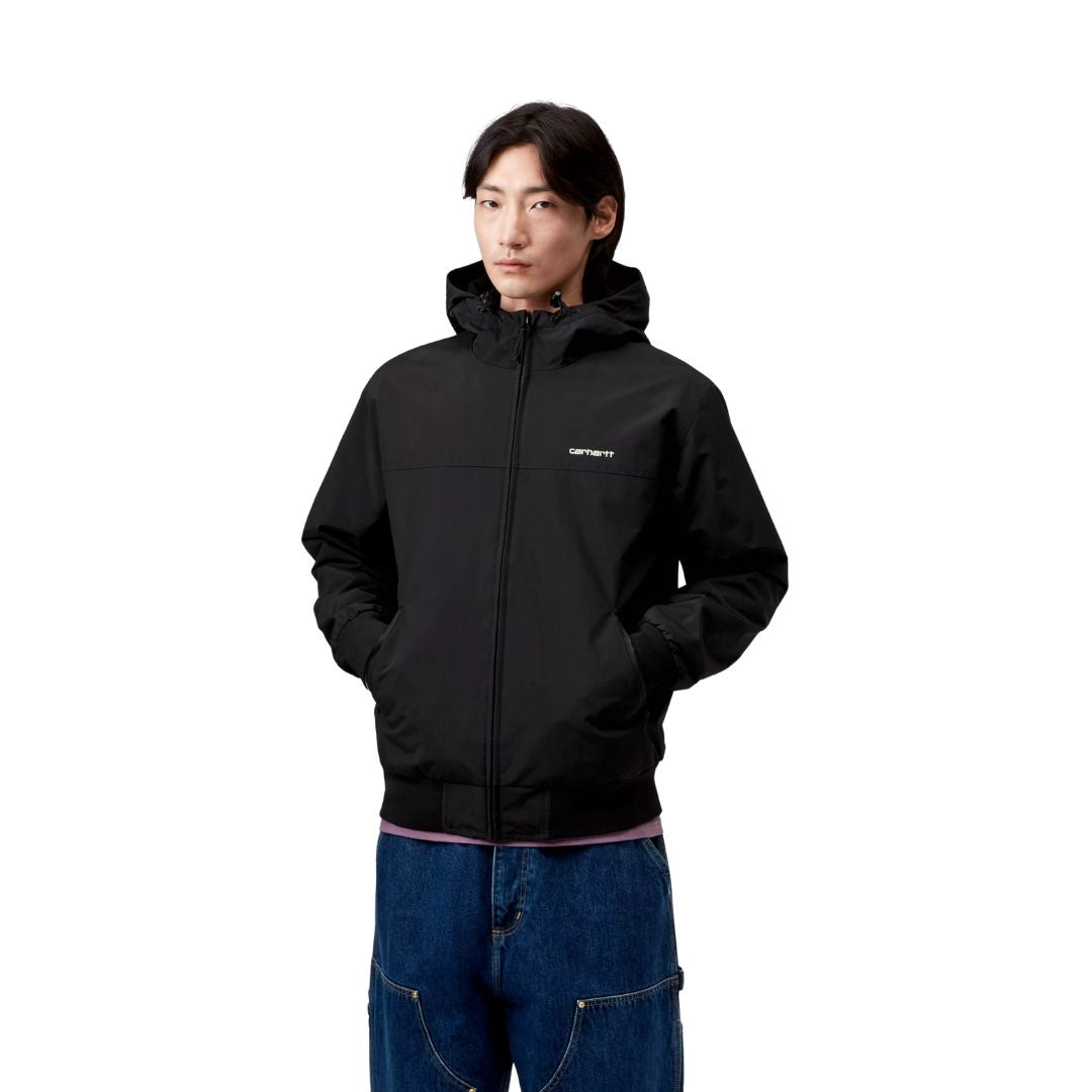 Modelo posando con la chaqueta Carhartt WIP Hooded Sail Jacket negra, con las manos en los bolsillos y capucha ajustada.