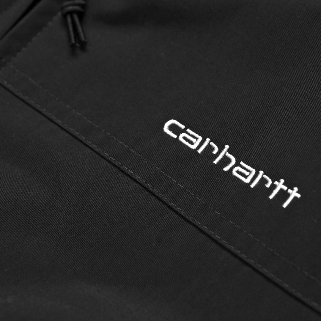 Detalle del logotipo bordado Carhartt en color blanco sobre la chaqueta Hooded Sail Jacket negra.