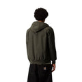 Vista trasera de la chaqueta Hooded Sail Cypress, con capucha, costura de yoke en la espalda y cintura acanalada, sobre pantalón negro con la etiqueta Carhartt WIP en el bolsillo.