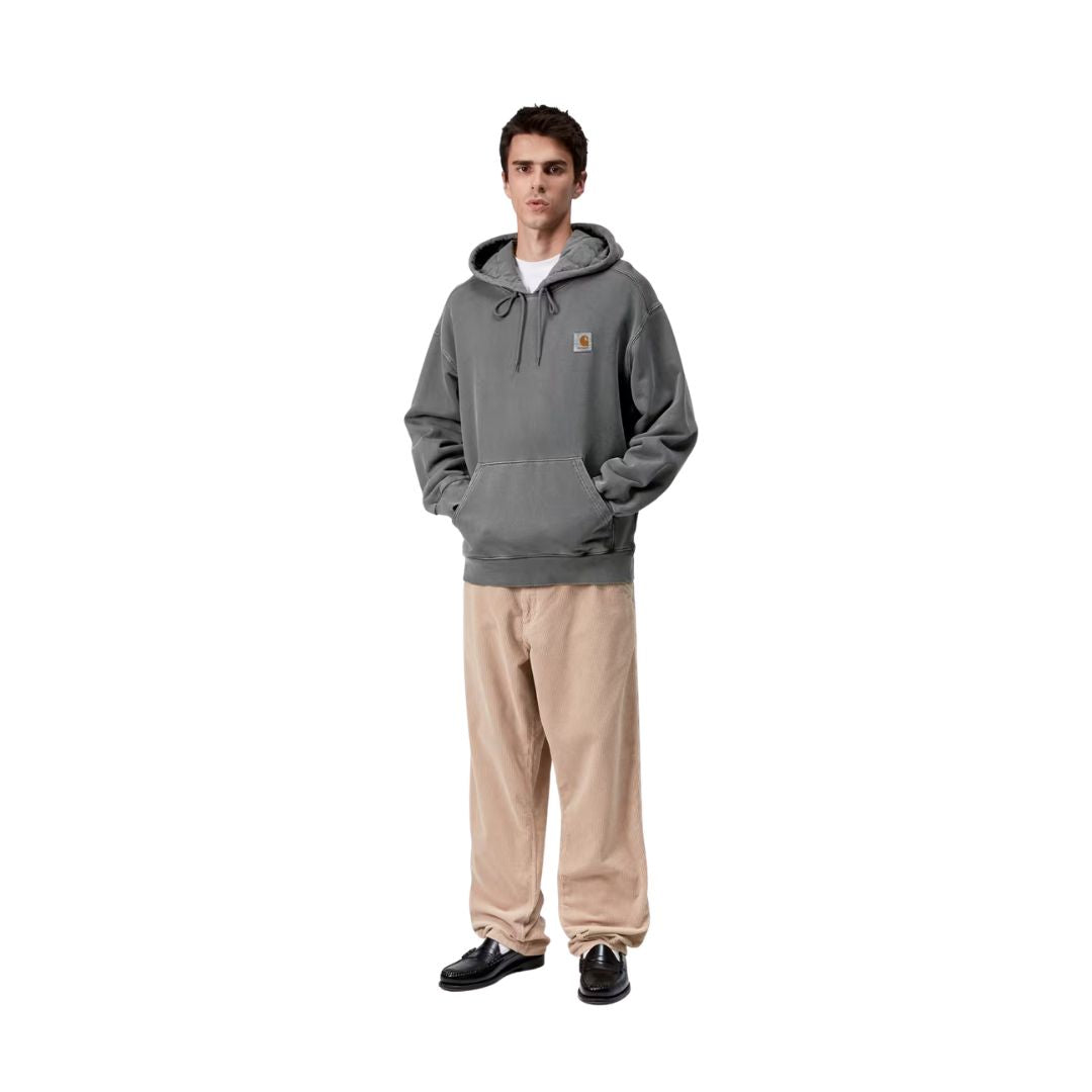 Modelo con la Carhartt WIP Hooded Vista Sweat en color negro garment dyed y pantalón de pana beige, mostrando de cuerpo entero el corte oversize y la capucha con forro guateado.