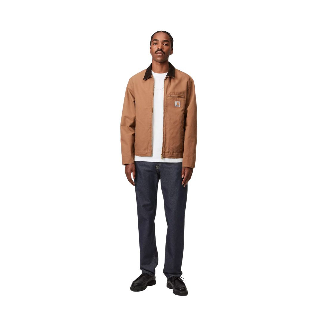 Modelo con pantalón vaquero carhartt wip klondike pant azul denim lavado combinado con chaqueta marrón.