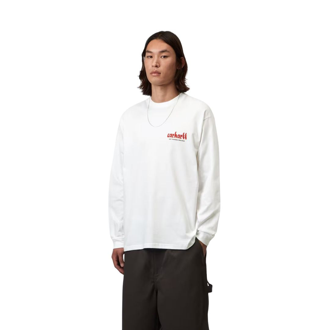 Carhartt WIP L/S Framework T-Shirt White en plano frontal sobre modelo con pantalón marrón oscuro, resaltando el pequeño estampado en rojo sobre el pecho.