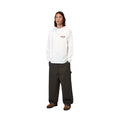 Carhartt WIP L/S Framework T-Shirt White combinada en look completo con pantalón marrón oscuro, mostrando el estampado frontal y la caída holgada de la manga larga.