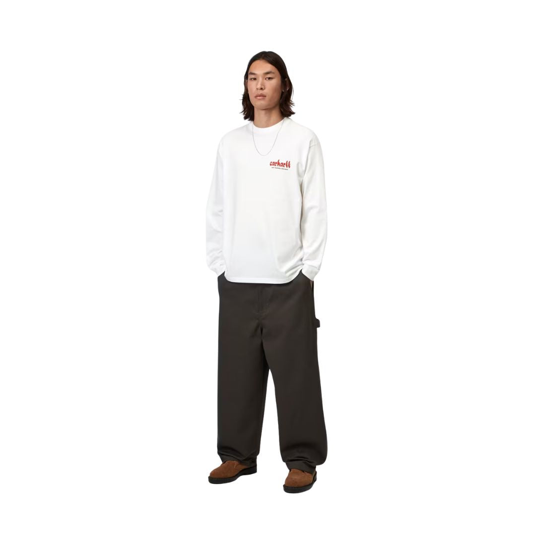 Carhartt WIP L/S Framework T-Shirt White combinada en look completo con pantalón marrón oscuro, mostrando el estampado frontal y la caída holgada de la manga larga.