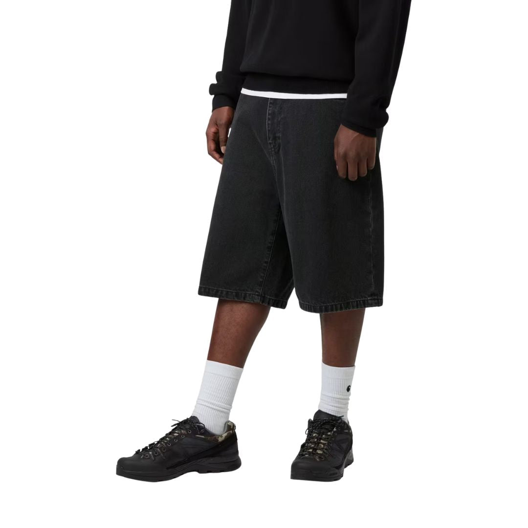 Carhartt WIP Landon Short negro lavado a la piedra, modelo vista lateral frontal, caída holgada y largo hasta rodilla con denim algodón pesado.